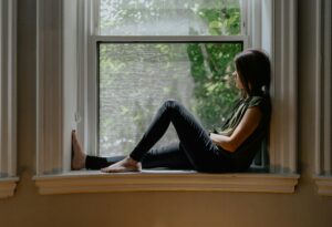 Woman sitting on window sill gazing outdoors